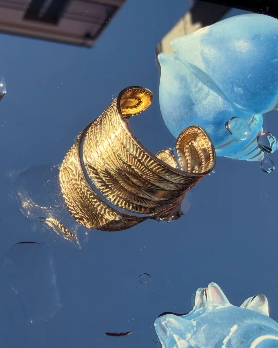 Bague La Solaire ton or posée sur un miroir reflétant un ciel bleu profond