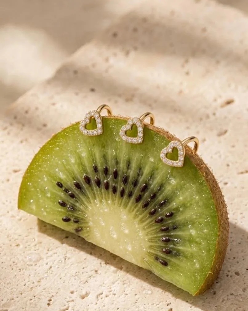 Trois faux piercings Lovely en forme de cœur pavé de zircones, posés sur une tranche de kiwi